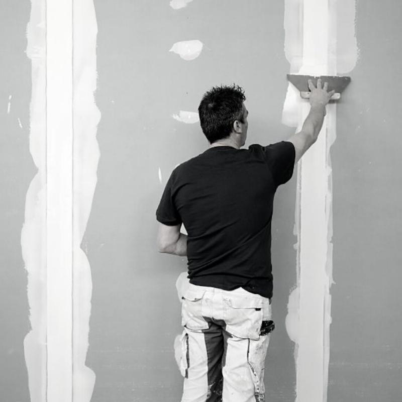 Artisan français réparant un mur avec peinture cloquée, utilisant des outils traditionnels